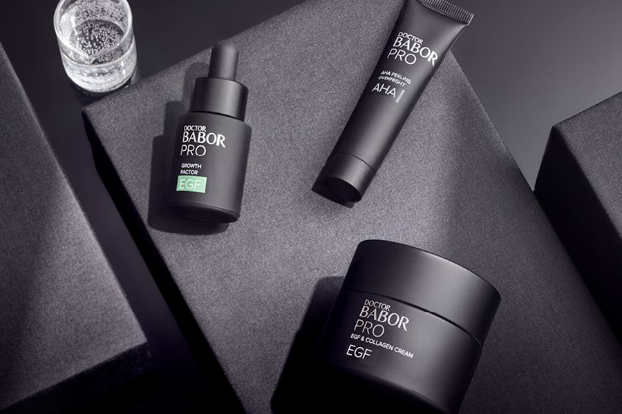 Drei elegante Doctor BABOR PRO Produkte &ndash; Serum, Peeling und Creme &ndash; stilvoll auf grauen Boxen arrangiert.