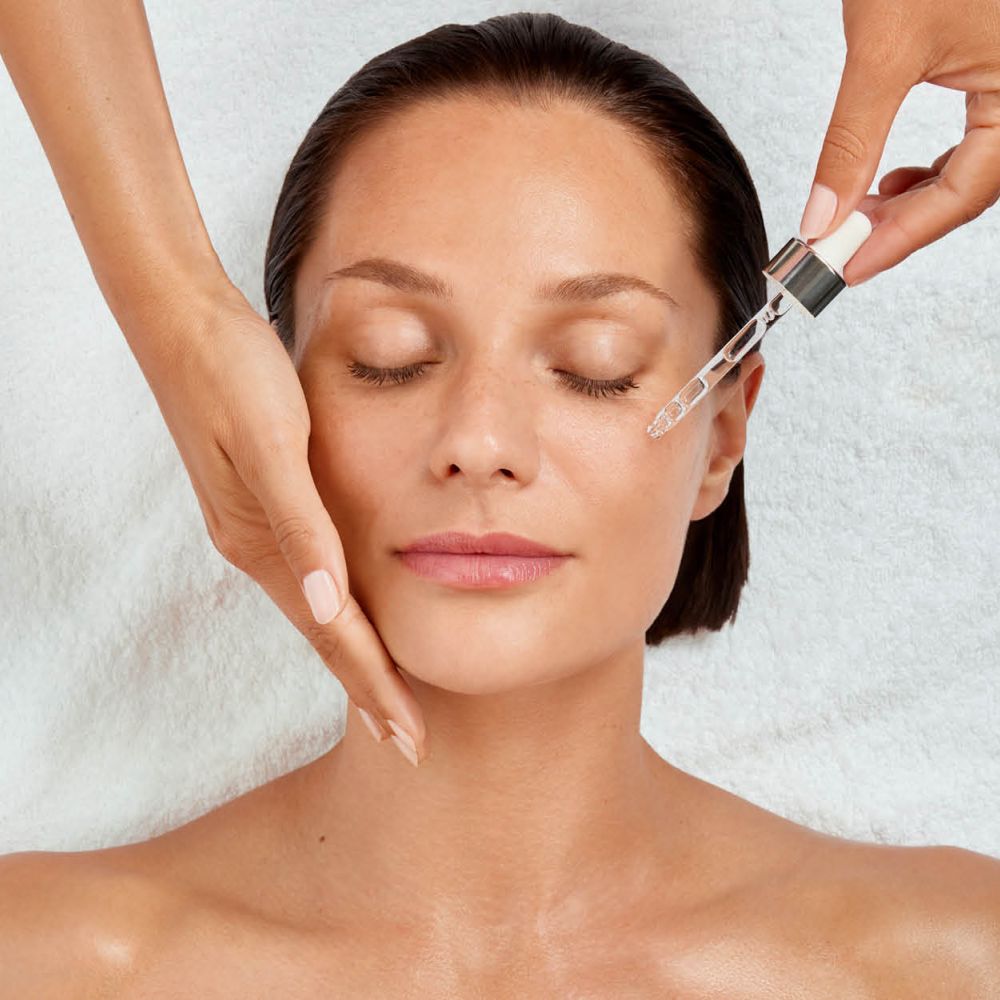 Frau mit geschlossenen Augen, Hand st&uuml;tzt die Wange, Pipette tr&auml;ufelt Serum aufs Gesicht