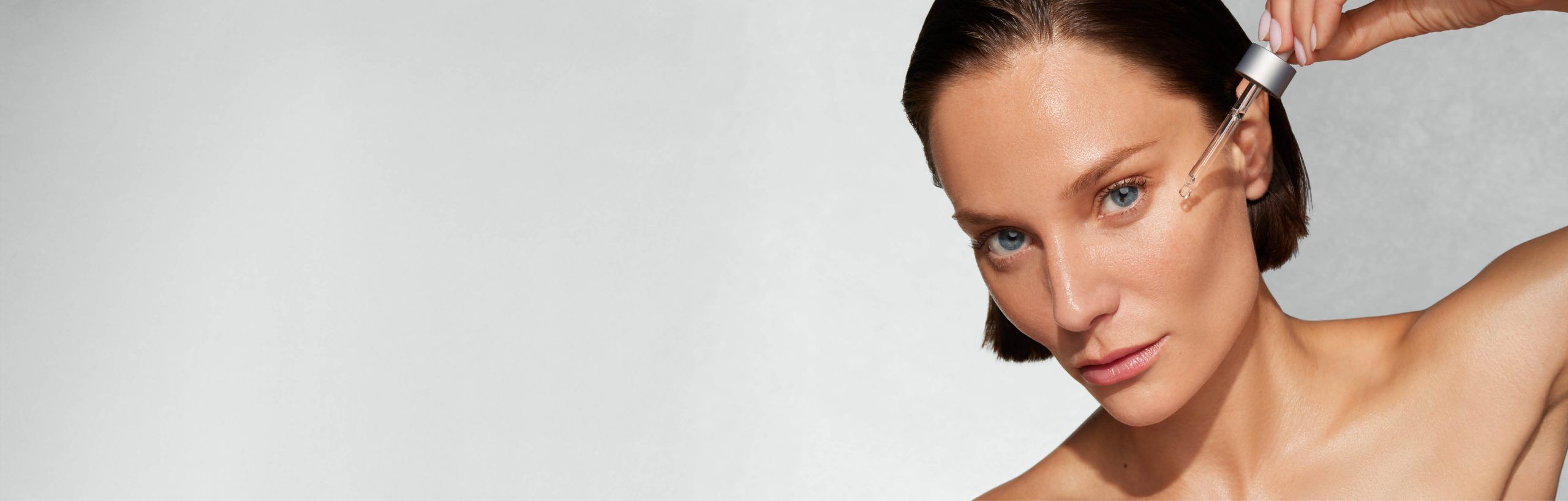 Frau mit erhobenem Arm tr&auml;gt per Pipette Serum aufs Gesicht.