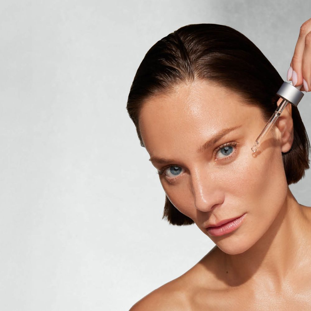 Frau mit erhobenem Arm tr&auml;gt per Pipette Serum aufs Gesicht.